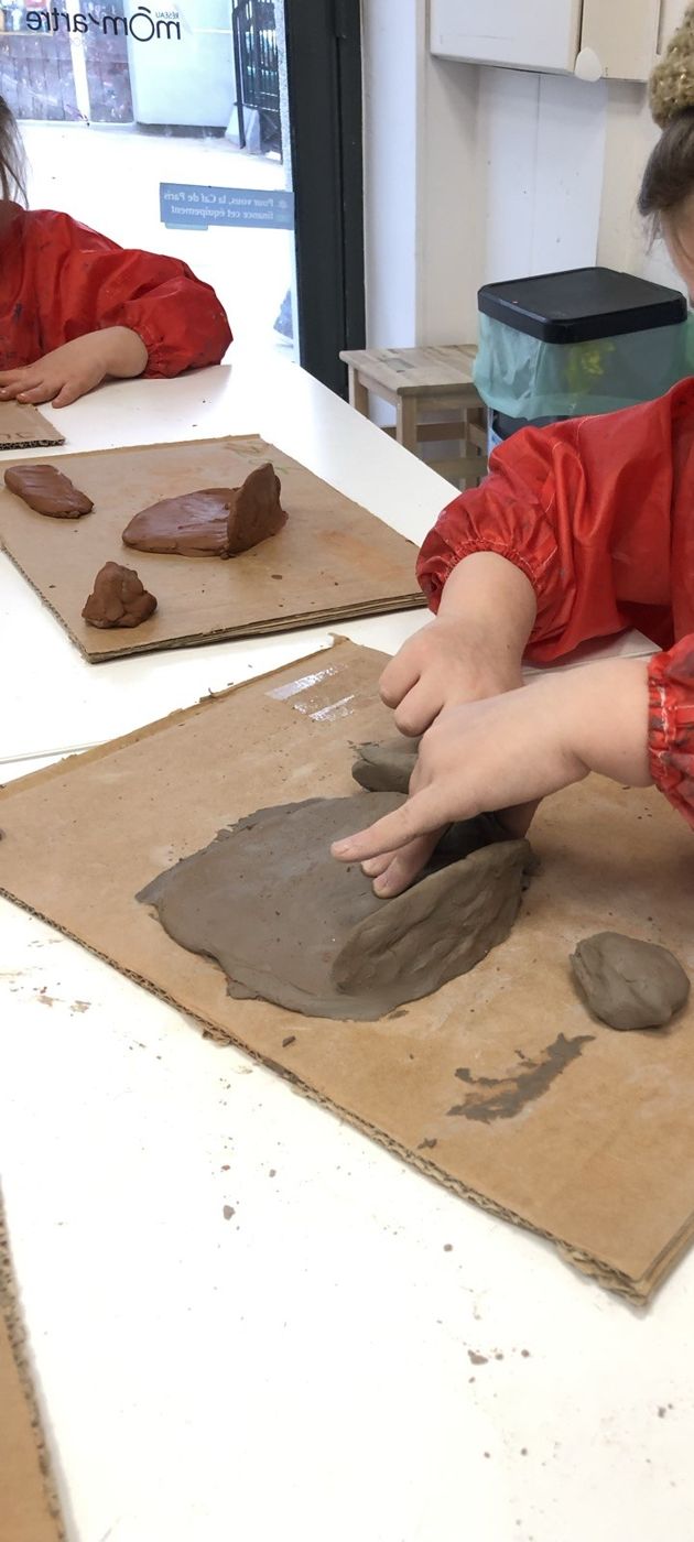 Une enfant aplatit l'argile sur une plaque de carton
