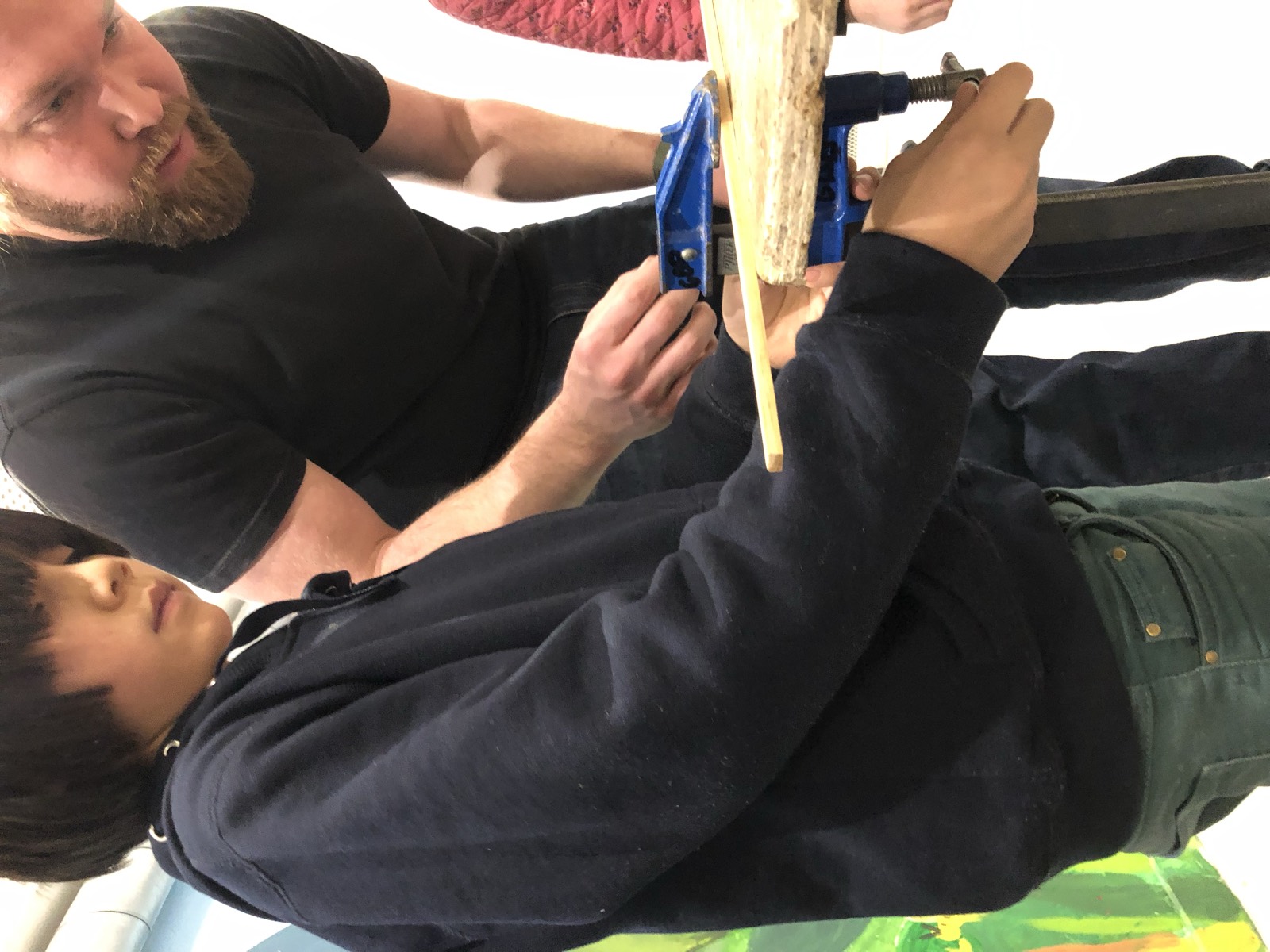 Un adulte guide un enfant qui scie une planche
